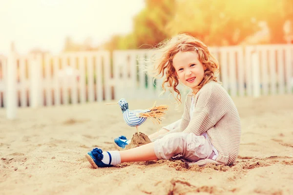 Happy child girl playing with toy bird on the beach on summer vacation — Stock Photo, Image