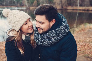 happy couple in warm knitted hat and scarf walking outdoor in autumn forest, cozy mood