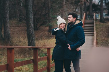 happy couple in warm knitted hat and scarf walking outdoor in autumn forest, cozy mood