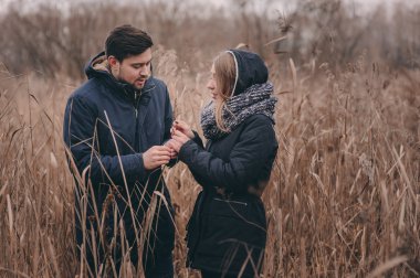 happy couple in warm knitted hat and scarf walking outdoor in autumn forest, cozy mood