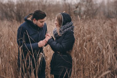 happy couple in warm knitted hat and scarf walking outdoor in autumn forest, cozy mood