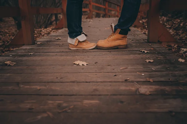 Boots of young loving couple walking outdoor on wooden bridge in autumn — 图库照片