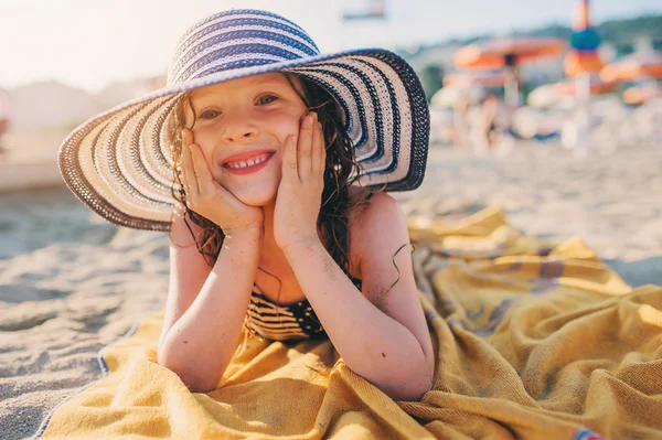 Niño feliz en traje de baño relajarse en la playa de verano, acostado en la toalla y broncearse un poco. Clima cálido, ambiente acogedor. Viajando en vacaciones de verano. Enfoque selectivo . — Foto de Stock