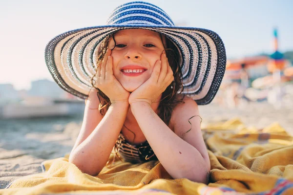 Niño feliz en traje de baño relajarse en la playa de verano, acostado en la toalla y broncearse un poco. Clima cálido, ambiente acogedor. Viajando en vacaciones de verano. Enfoque selectivo . — Foto de Stock