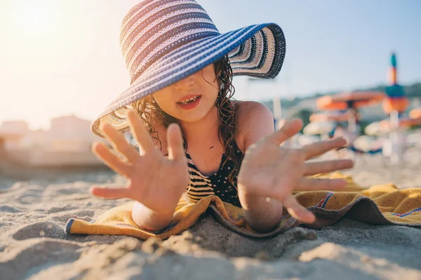 Niño feliz en traje de baño relajante en la playa de verano, acostado sobre una toalla y jugando con la arena. Clima cálido, ambiente acogedor. Viajar en vacaciones de verano . — Foto de Stock