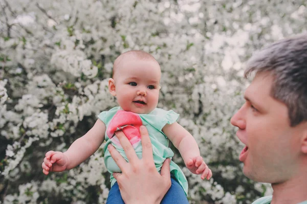 Família amorosa feliz com a filha do bebê no jardim de primavera florescendo. Pai segurando menina. Passar tempo juntos ao ar livre — Fotografia de Stock