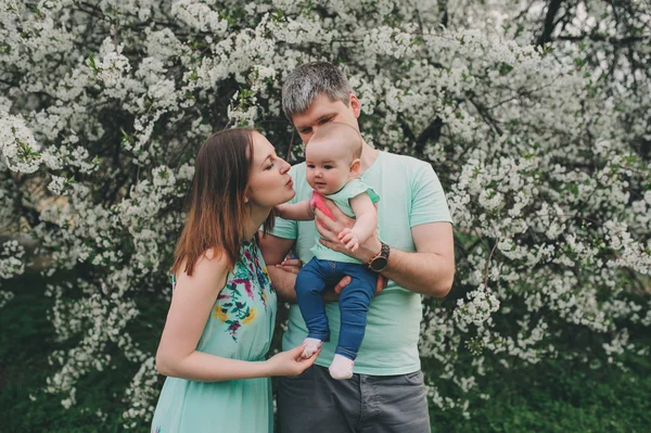 Família amorosa feliz com a filha do bebê no jardim de primavera florescendo. Pai segurando menina. Passar tempo juntos ao ar livre — Fotografia de Stock