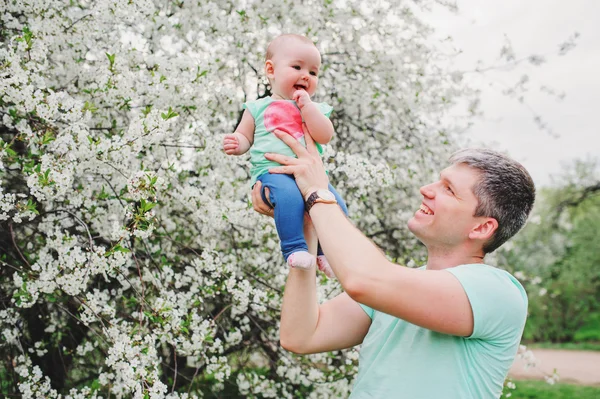 Família amorosa feliz com a filha do bebê no jardim de primavera florescendo. Pai segurando menina. Passar tempo juntos ao ar livre — Fotografia de Stock