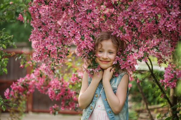 Happy child girl in dress playing near blooming tree in spring garden. Rural cozy scene, outdoor seasonal activities. — Stock Photo, Image