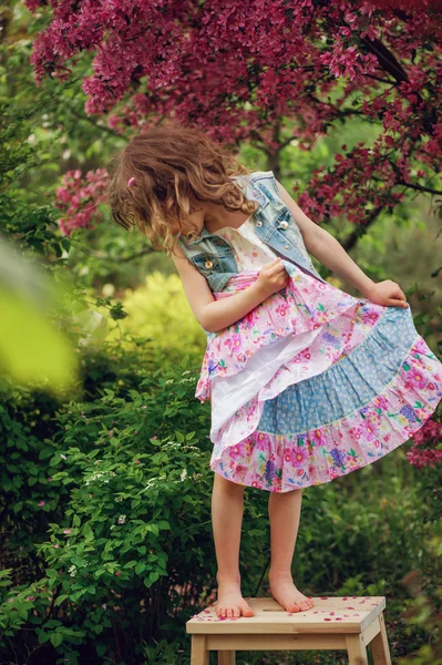 Çiçek açan ağaç bahar bahçe yakınındaki oynarken elbiseli kız mutlu bir çocuk. Kırsal rahat sahne, mevsimlik açık hava etkinlikleri. — Stok fotoğraf