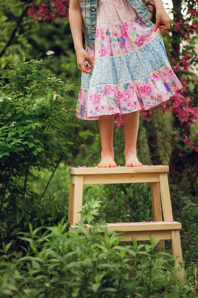 Niña feliz en vestido jugando cerca del árbol en flor en el jardín de primavera. Rural ambiente acogedor, actividades de temporada al aire libre . —  Fotos de Stock