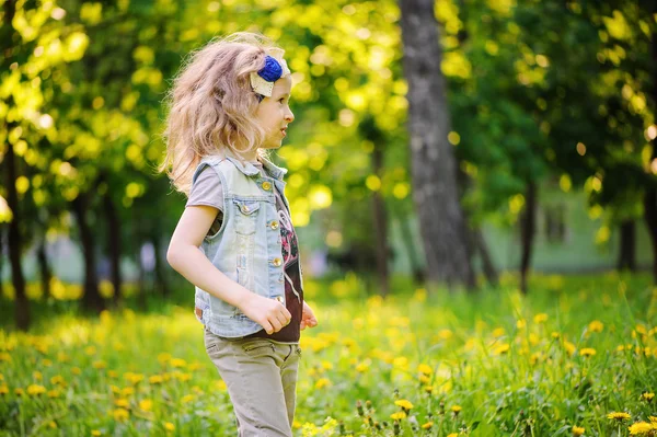 Glückliches Kind Mädchen spielt auf bunten Frühlingswiese. blühende Löwenzahne im Hintergrund, saisonale Aktivitäten im Freien. wohlig warme Stimmung. — Stockfoto