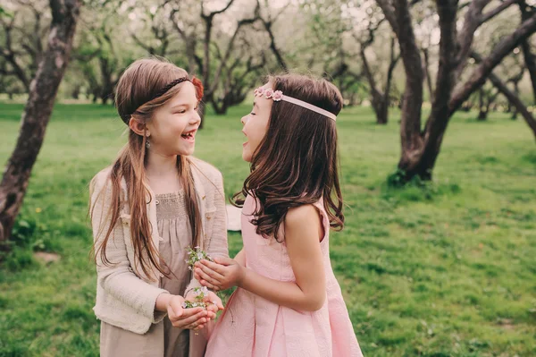 Zwei glückliche kleine Freundinnen, die im Frühlingsgarten Blumen pflücken. Schwestern verbringen Zeit miteinander im Freien. Saisonale Aktivitäten. — Stockfoto