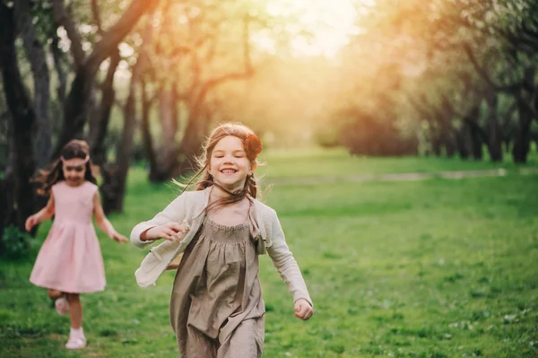 Bahar bahçe içinde çalışan iki mutlu küçük kız arkadaşım. Birlikte vakit kız çocuk açık ve oyun. Yürüyüşte mevsimsel faaliyetler — Stok fotoğraf