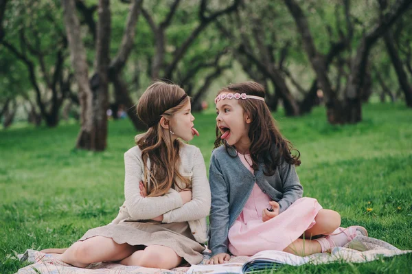Two kid girlfriends showing tongue to each other on the walk in spring. Upset angry sisters. Outdoor activities. — Stock Photo, Image