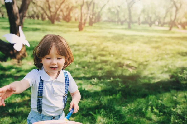 快乐与弹簧网蹒跚学步的男孩抓蝴蝶在花园里散步。户外季节性活动. — 图库照片