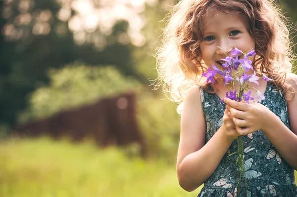 Ragazza felice bambino che gioca con mazzo di campanule in estate. Buona infanzia, attività all'aria aperta. Esplorare la natura e raccogliere fiori. Accoglienti vacanze paese . — Foto Stock