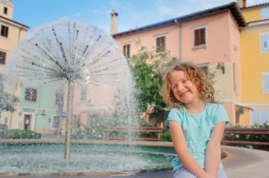 child girl relaxing at fountain in Izola (Isola) city in Slovenia. Traveling in Europe on summer vacation