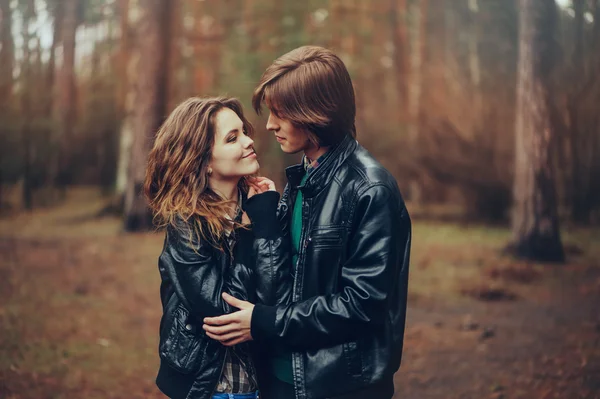 Młoda para kochających szczęśliwy w kurtki skórzane przytula odkryty na przytulne spacer w lesie — Zdjęcie stockowe