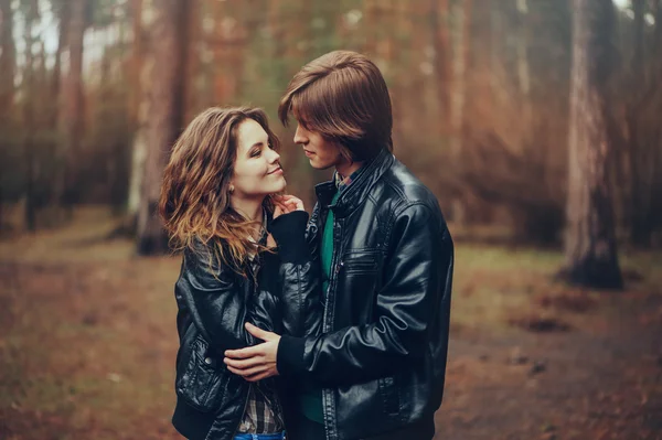 Joven feliz amante pareja en chaquetas de cuero abrazos al aire libre en acogedor paseo en el bosque —  Fotos de Stock