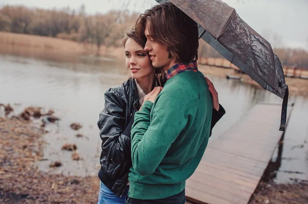 Feliz jovem casal amoroso escondido sob guarda-chuva na primavera chuvoso passeio no campo — Fotografia de Stock