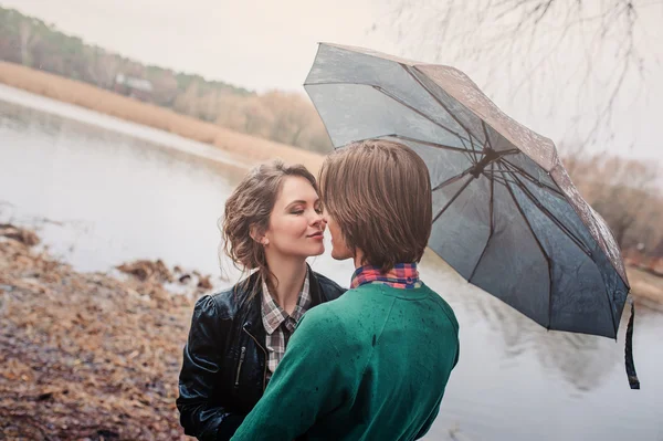 Feliz jovem casal amoroso escondido sob guarda-chuva na primavera chuvoso passeio no campo — Fotografia de Stock