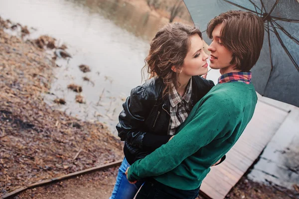 Felice giovane coppia amorevole che si nasconde sotto l'ombrello in primavera passeggiata piovosa sulla campagna — Foto Stock