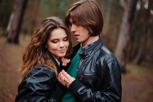 Heureux couple amoureux en vestes en cuir marchant en plein air. Jeune copain et petite amie câlins et baisers dans la forêt — Photo