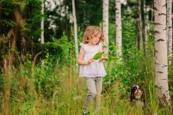 Söta barn flicka som leker med lämnar i sommar skogen med sin hund. Natur utforskning med barn. Landsbygdens utomhusaktiviteter. — Stockfoto