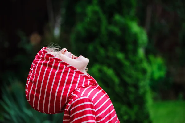 Bambina in impermeabile rosso passeggiando nel giardino estivo piovoso. Attività all'aperto stagionali — Foto Stock