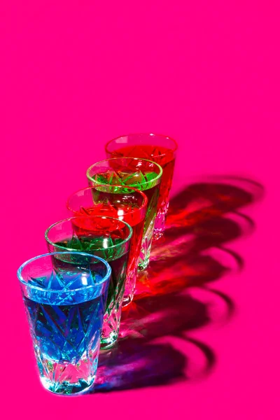 Multicolored shot glasses with Strong alcohol on pink background — Stock Photo, Image