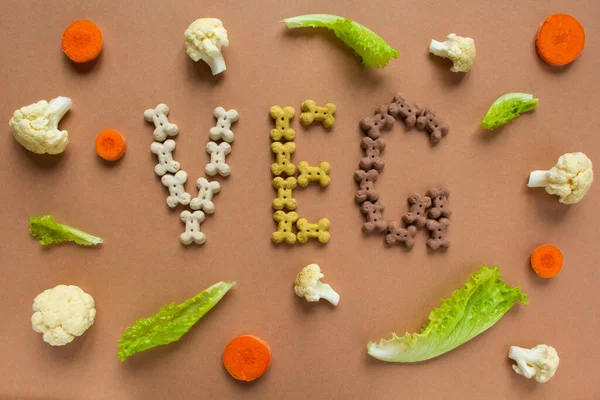 Cane vegetariano crocchette secche in forma di osso con verdure su sfondo beige. Lettering VEG. — Foto Stock