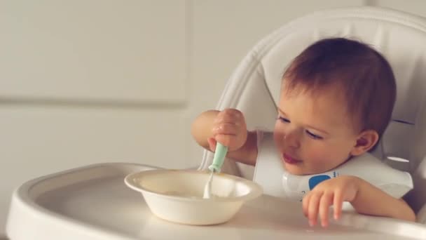Menina bonito bebê comendo comida de bebê com colher na cadeira alta na cozinha em casa — Vídeo de Stock