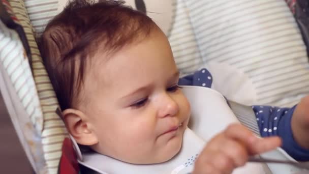 Menina bonito comendo comida de bebê com as mãos na cadeira alta na cozinha da casa. Close-up — Vídeo de Stock