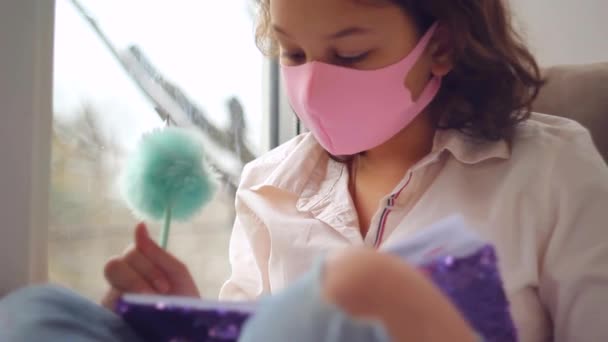 Schoolgirl in medical mask writing homework at home. Education and distance learning concept — Stock Video