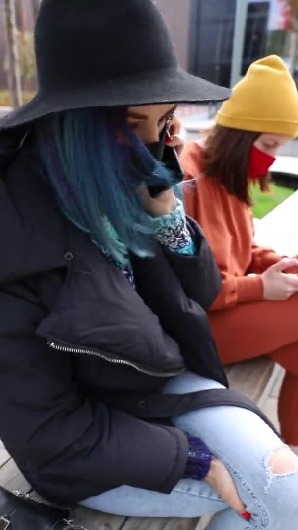 Studentki w maskach ochronnych i kapeluszu rozmawiające przez telefon na zewnątrz. Pionowe wideo — Wideo stockowe