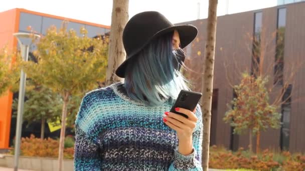 保護黒マスクの青い髪の女の子とスマートフォンで帽子。都会のファッション. — ストック動画