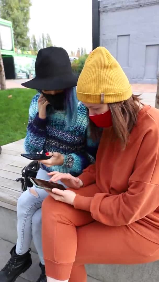 2 amigas en mascarilla médica protectora con smartphones afuera. Vídeo vertical — Vídeo de stock