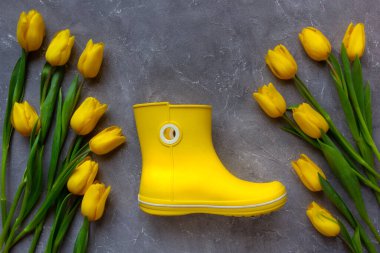 Sarı laleler ve gri arka planda sarı lastik çizmeler. Moda rengi 2021.