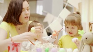 Mutlu Paskalyalar. Bir anne ve iki küçük kızı evcil mutfakta paskalya yumurtası boyuyor.