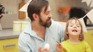 Mutlu Paskalyalar. Bir baba ve kızı evdeki mutfakta paskalya yumurtası boyuyor.