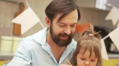 Mutlu Paskalyalar. Bir baba ve kızı evdeki mutfakta paskalya yumurtası boyuyor.