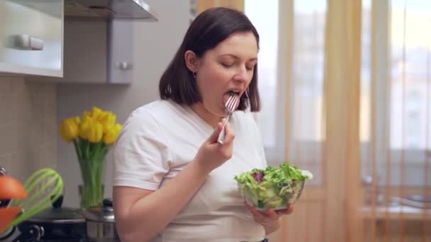 Ulykkelig overvægtig kvinde støbning forsøger at tygge salat i køkkenet – Stock-video