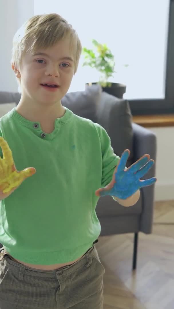 Menino com Síndrome de Down com tinta amarela e azul nas mãos. Vídeo em formato vertical — Vídeo de Stock