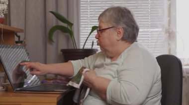 Yaşlı bir kadın dizüstü bilgisayarda nakış işliyor..