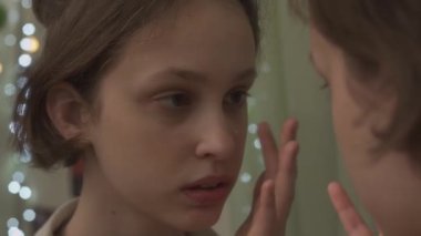 Genç bir kızın aynaya bakarak nemlendirici krem sürdüğü yakın plan.