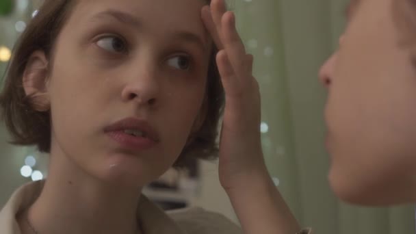 Счастливая девочка-подросток наносит увлажняющий крем, глядя в зеркало — стоковое видео