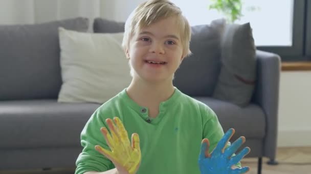 Menino feliz com síndrome de Down com tinta amarela e azul nas mãos — Vídeo de Stock