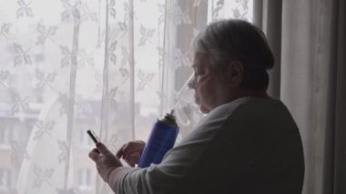 Oksijen maskeli yaşlı kadın cep telefonunu arıyor.