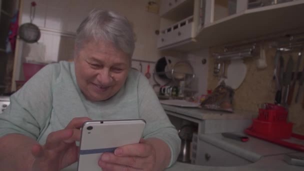 Старшая женщина со смартфоном смеется над домашней кухней — стоковое видео